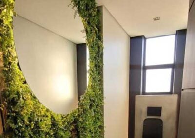 Round bathroom mirror set within a lush green feature wall above a basin