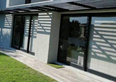 Black-framed glass doors beneath a slatted canopy overlooking a residential garden