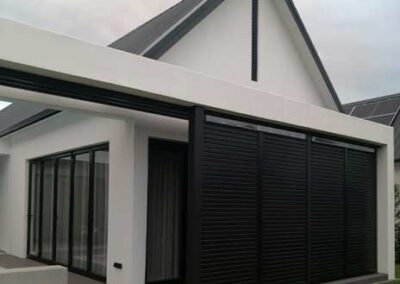 Black louvred panels enclosing a covered patio beside a modern home