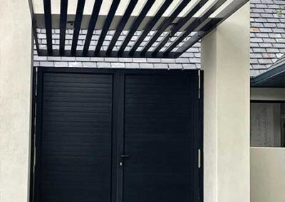 Black louvred double doors beneath a matching slatted entrance canopy.