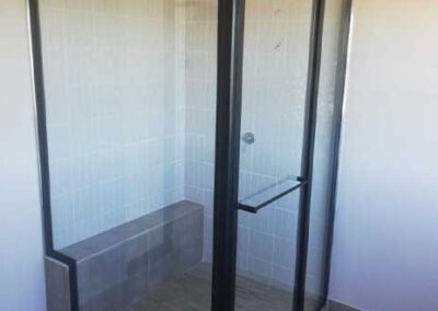 Black-framed glass shower enclosure with hinged entry and tiled interior