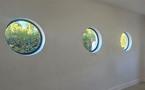 Three circular glass openings set into a light interior wall.