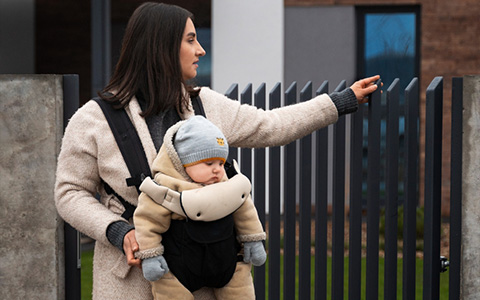 Woman carrying a baby while opening a black vertical-bar entrance
